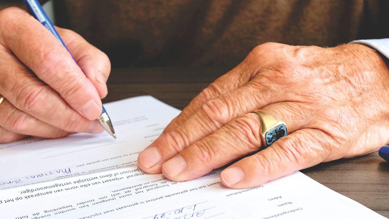 Manos de una persona mayor firmando un documento